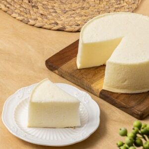 Queso artesano fresco sobre tabla de madera con porción servida en plato blanco